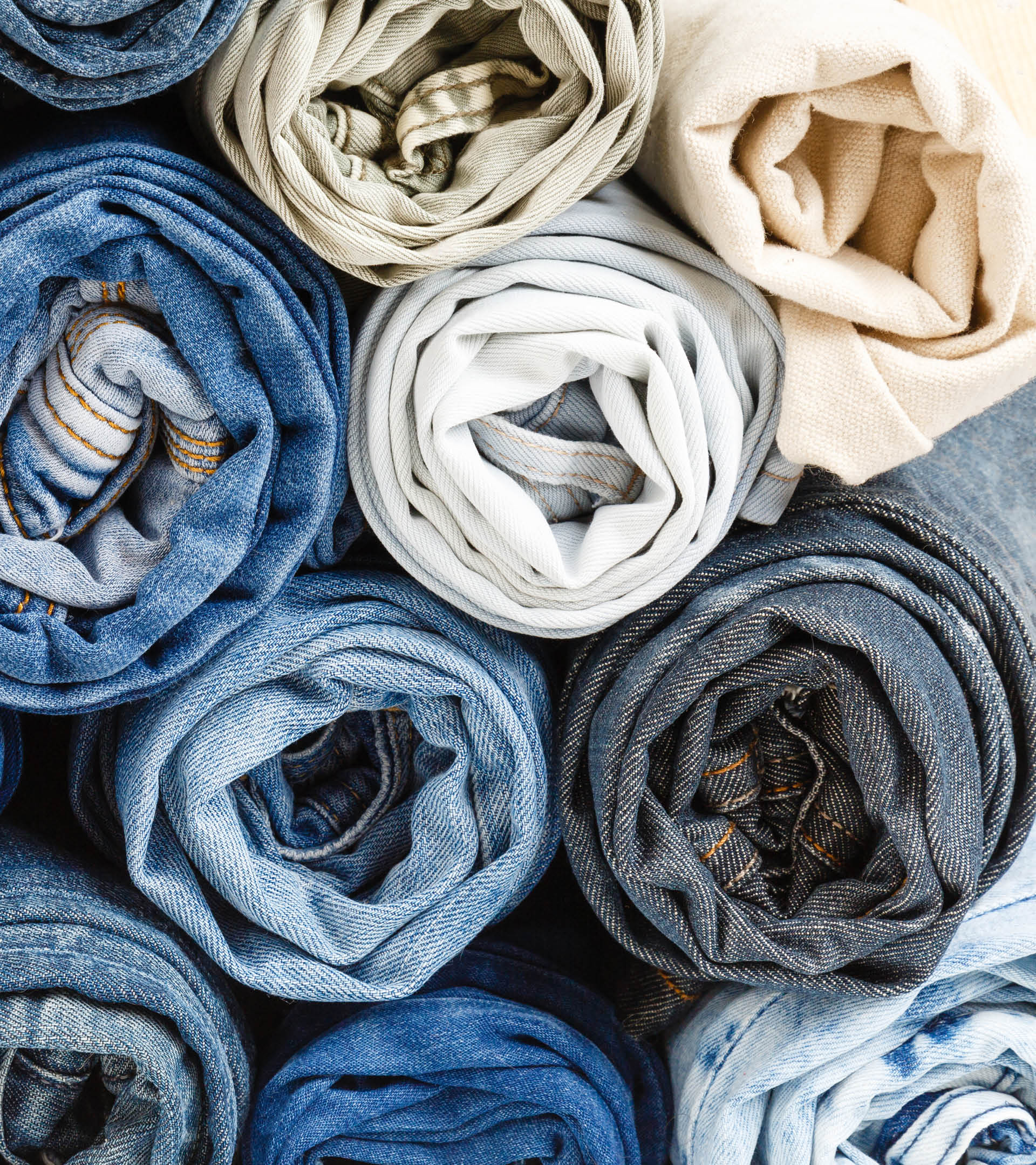 background from stack of different rolled jeans. Roll blue denim jeans arranged in stack. Jeans pyramid. Recycling old blue jeans on wooden table. Denim upcycle. Zero waste