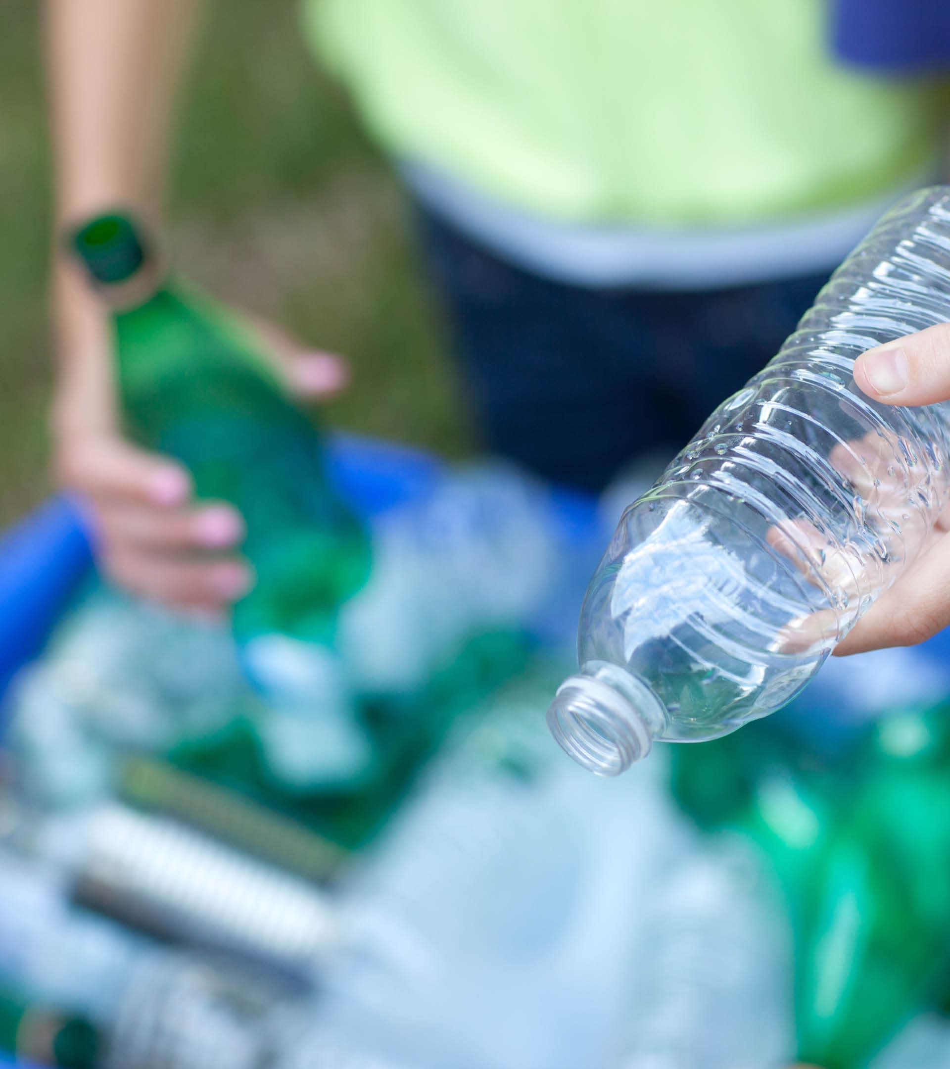 Caucasian boy and girl putting clear and green bottles and metal cans in recycling blue bin outside in yard